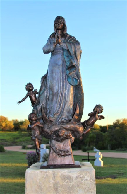 Bronze statue of Our Lady of the Rosary in prayer, attended by cherubs, on the cemetery grounds